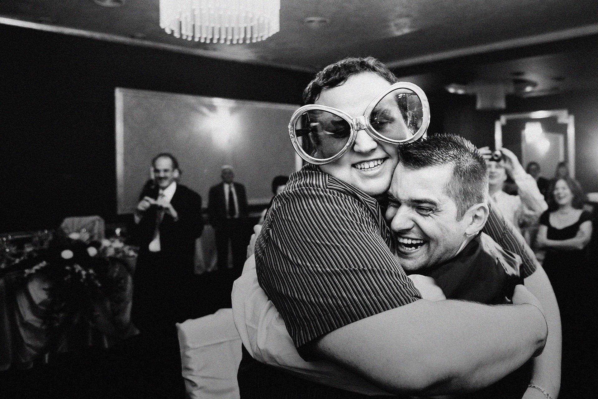 Mirele și cel mai bun prieten – fotograf nuntă Transilvania Mirele îmbrățișat de un invitat care poartă ochelari haiosi la nuntă